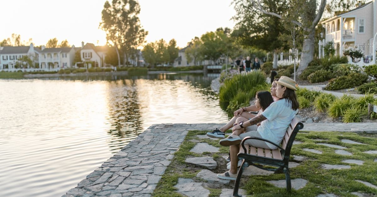 Two women sitting on a lakeside bench enjoying a serene sunset view.