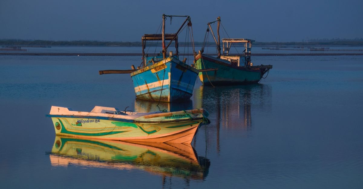 Serene scene of colorful fishing boats reflecting on calm waters at sunset in Jaffna, Sri Lanka.