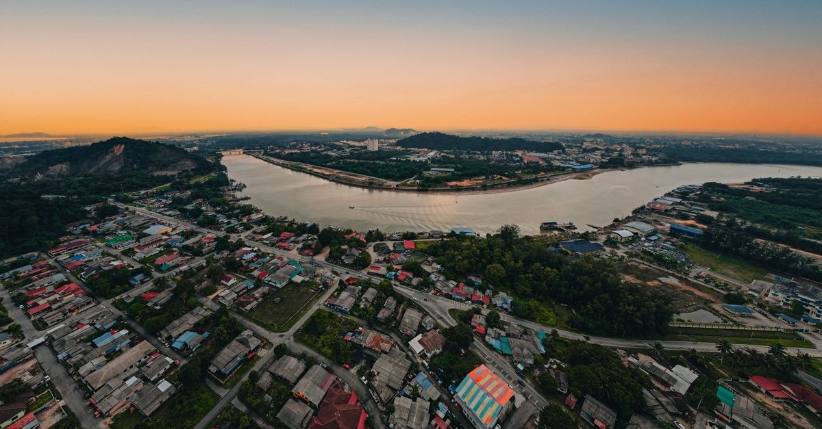 D’Resort @ Downtown East, Pasir Gudang: A Green Escape by Pasir Ris Park A breathtaking aerial view of a townscape by a river at sunset, showcasing colorful rooftops and serene water reflections.