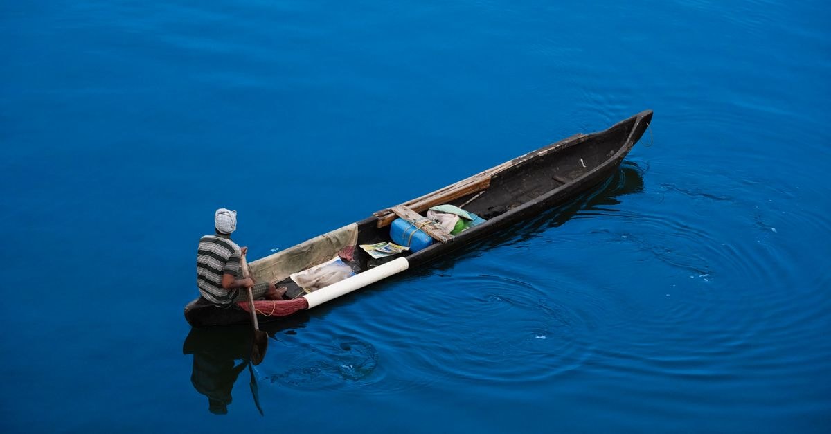 Kibuye travel guide: quiet corners on Lake Kivu A lone fisherman navigates his wooden canoe across tranquil blue waters, creating ripples in the serene setting.