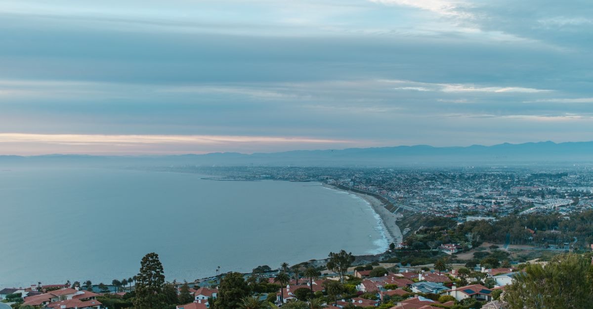 Aerial view of a coastal city at twilight with shoreline and cityscape.
