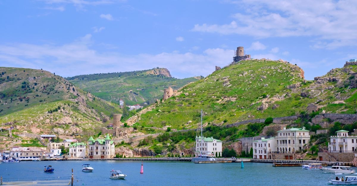 Naryan-Mar Travel Guide: Planning Tips, Costs and Things to Do Picturesque coastal town with boats, lush hills, and historical buildings under a clear blue sky.