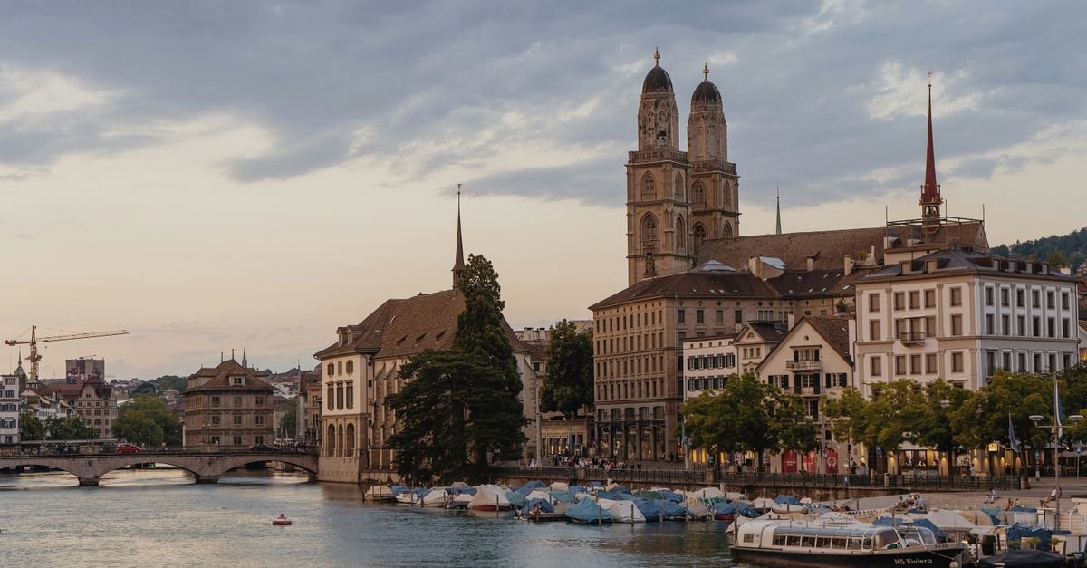 Zurich in July 2026: Things to Do, Costs and What to Expect Scenic Zurich cityscape featuring the Grossmünster church along the Limmat River at dusk.