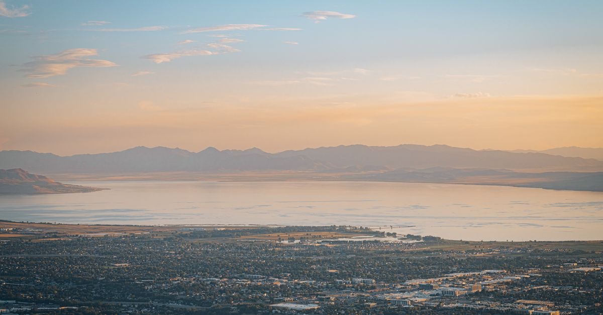 A breathtaking aerial view of a town by a serene lake at sunset, surrounded by vast plains and mountains.