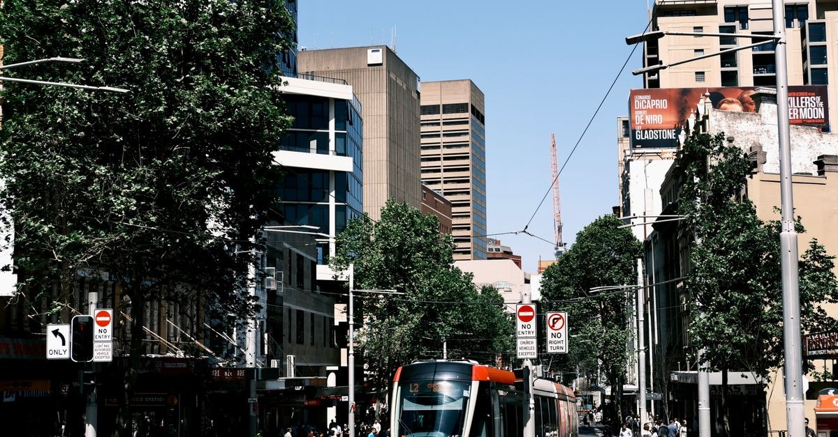 Adelaide Travel Guide: Culture, Markets, and Getting Around Urban scene with a tram navigating city streets amidst skyscrapers on a sunny day.