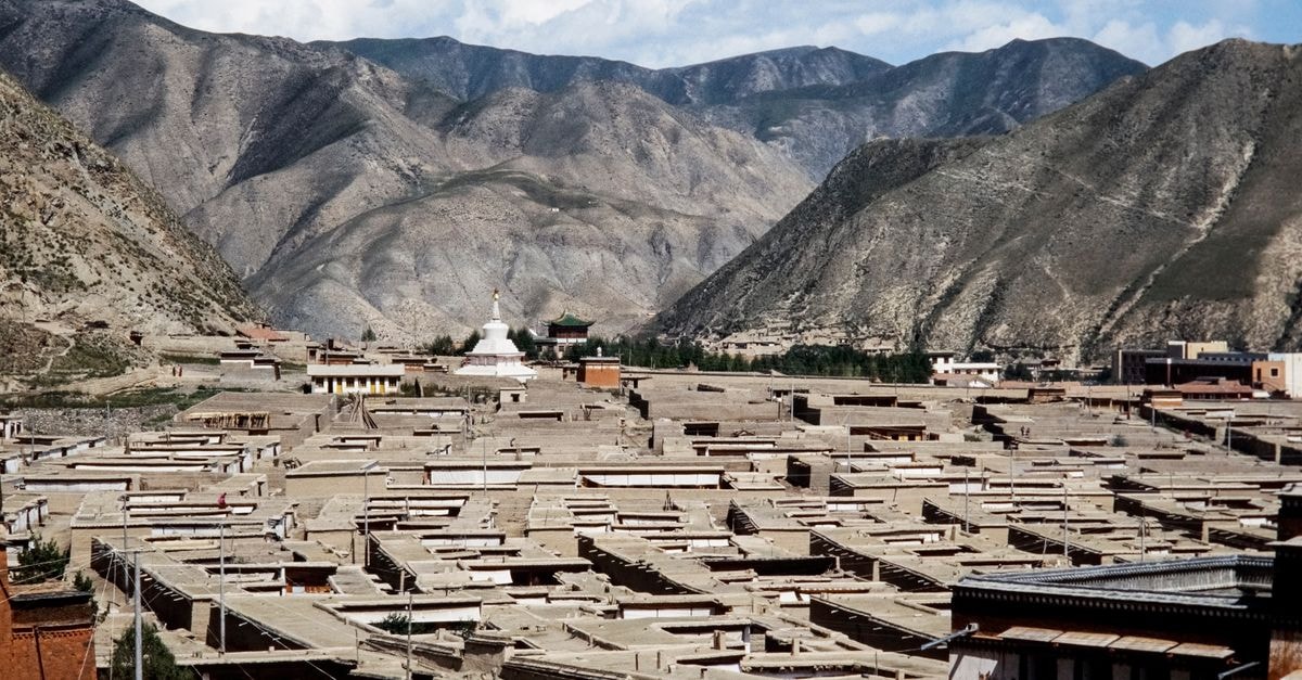 Tracing Silk Road Echoes in Wuwei: A Gansu Travel Guide An expanse of traditional Tibetan architecture set against the scenic mountains of China, under a clear sky.