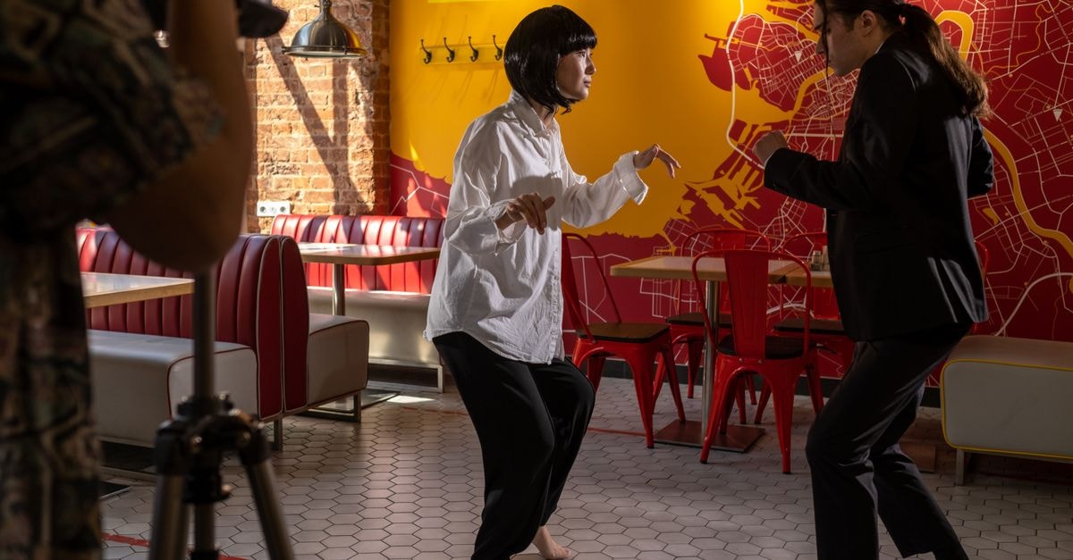 ‘Office Space’ Actor Richard Riehle Dies at 78 Actors rehearsing a scene in a colorful café during a film shoot. Engaging choreography and vibrant background.