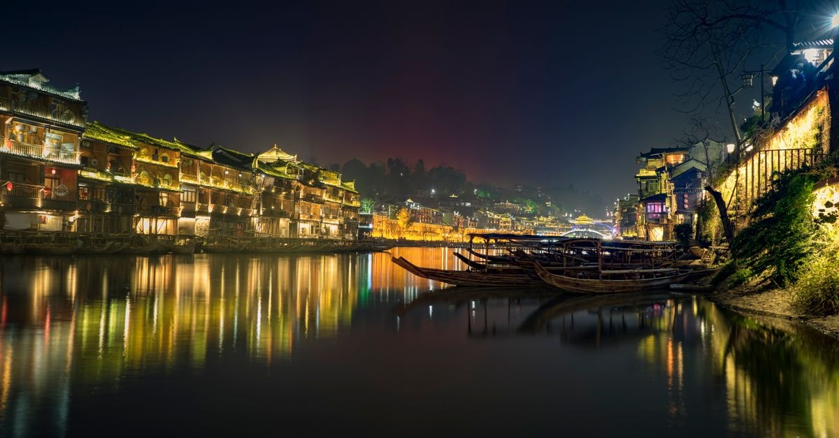 Illuminated Fenghuang Ancient Town with boats on the Tuo River at night