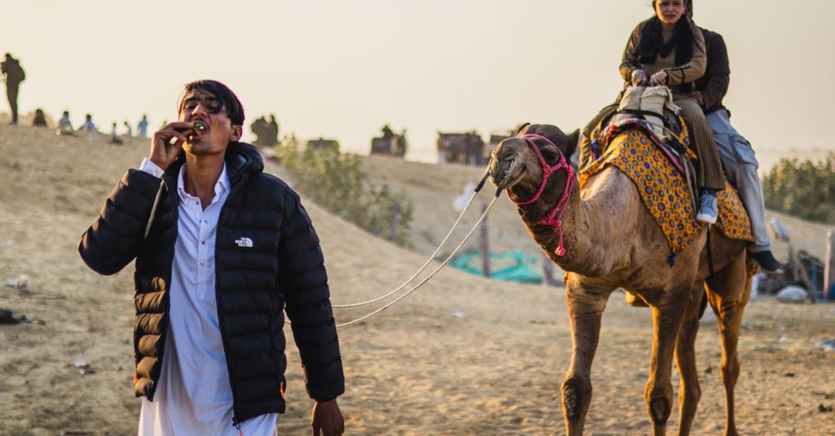Sukkur Travel Guide: Slow Days by the Indus A man leads a camel with riders through a desert during sunset.