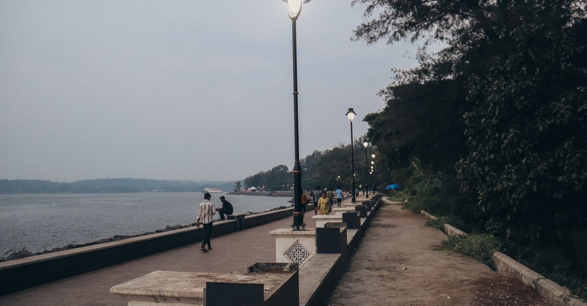 Kozhikode Travel Guide: Where the Coast Meets the Ghats A tranquil riverside promenade with streetlights, trees, and people walking.