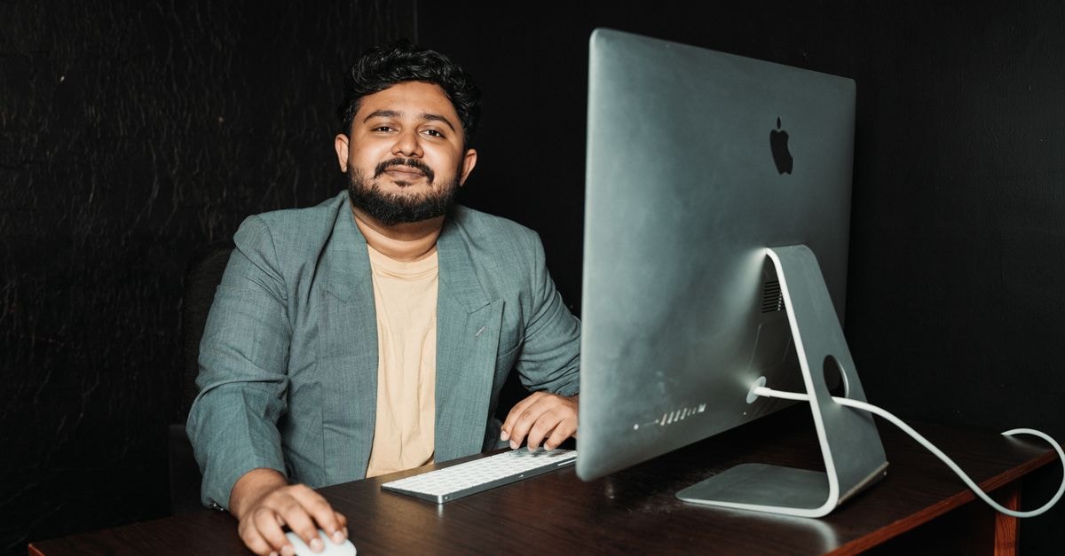 Smiling man in office attire working at a desk using a computer and wireless mouse.