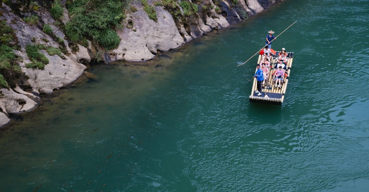 A group enjoying a serene bamboo raft ride on a turquoise river beside lush green cliffs.