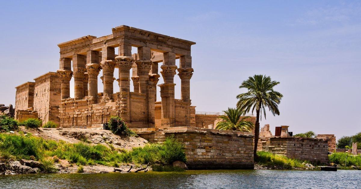 Ancient temple ruins near the Nile River with a palm tree and clear sky.