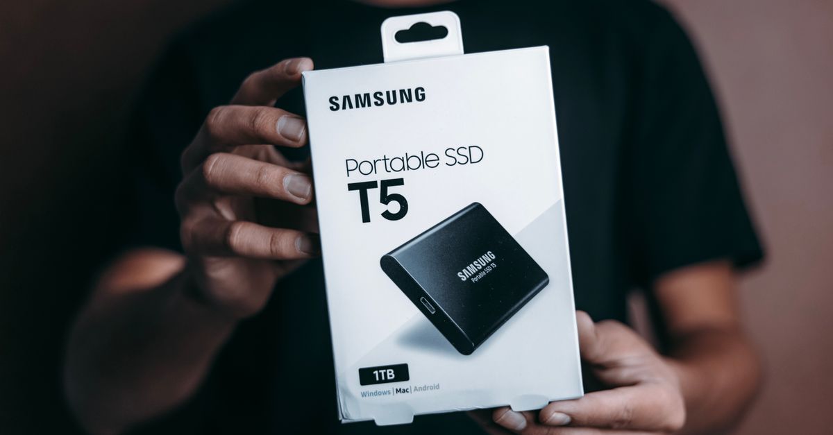 Samsung Faces Memory Rout as China CXMT Lists, Mulls Paid AI Tier Close-up of a person holding a Samsung T5 Portable SSD box, emphasizing modern technology.