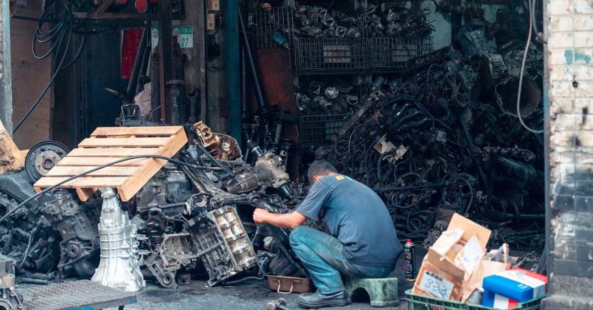 Xos, Inc.: A Pre-Profit EV Truck Maker Priced for Survival, Not Returns Mechanic fixing auto parts in a cluttered urban workshop, surrounded by machinery.