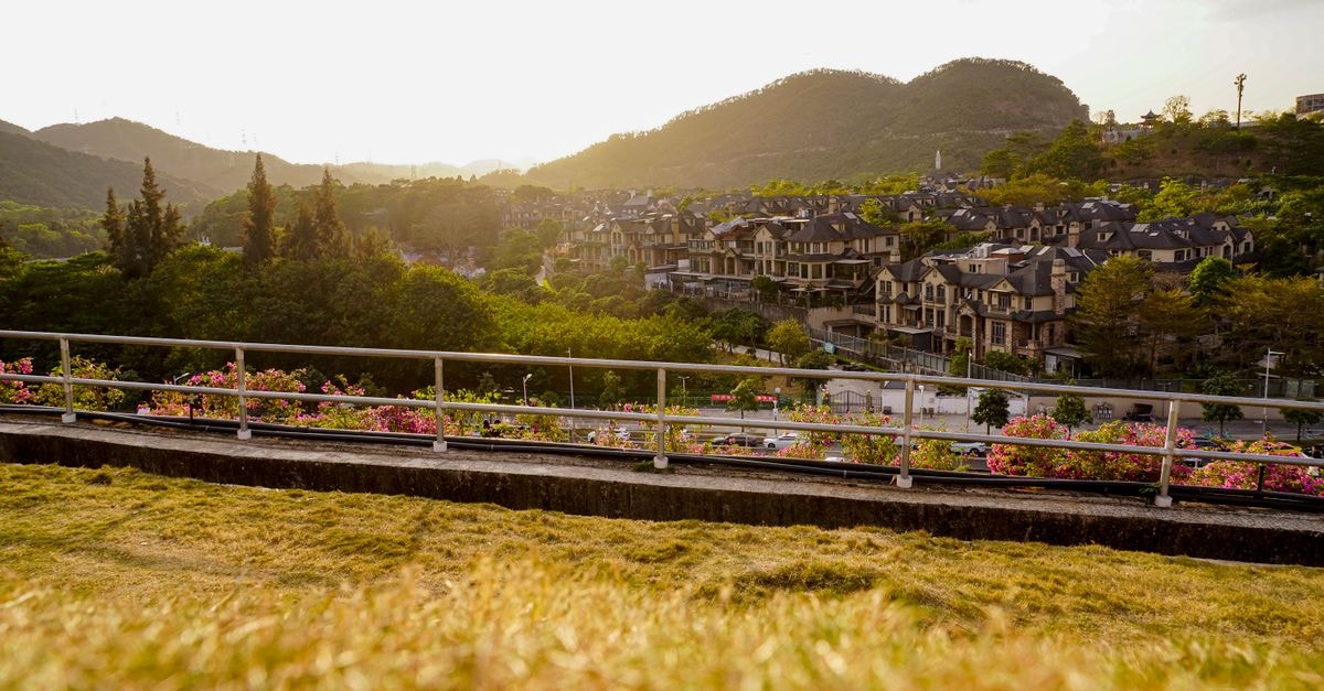 A Quiet Corner of Guangdong: Zhongshan Travel Guide A serene view of a hillside town in Shenzhen during sunset, capturing lush greenery and residential architecture.