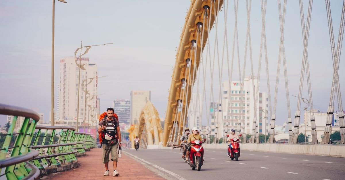 A man walking on the Dragon Bridge in Da Nang with motorbikes passing. Urban scene with city buildings.