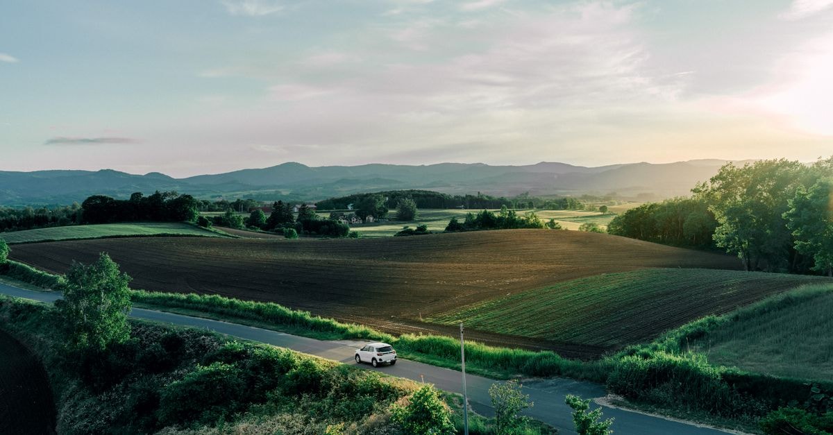 Furano Travel Guide: Quiet Fields, Local Cheese, and Slow Hokkaido Days Tranquil rural landscape in Hokkaido, Japan with a winding road, fields, and sunset horizon.