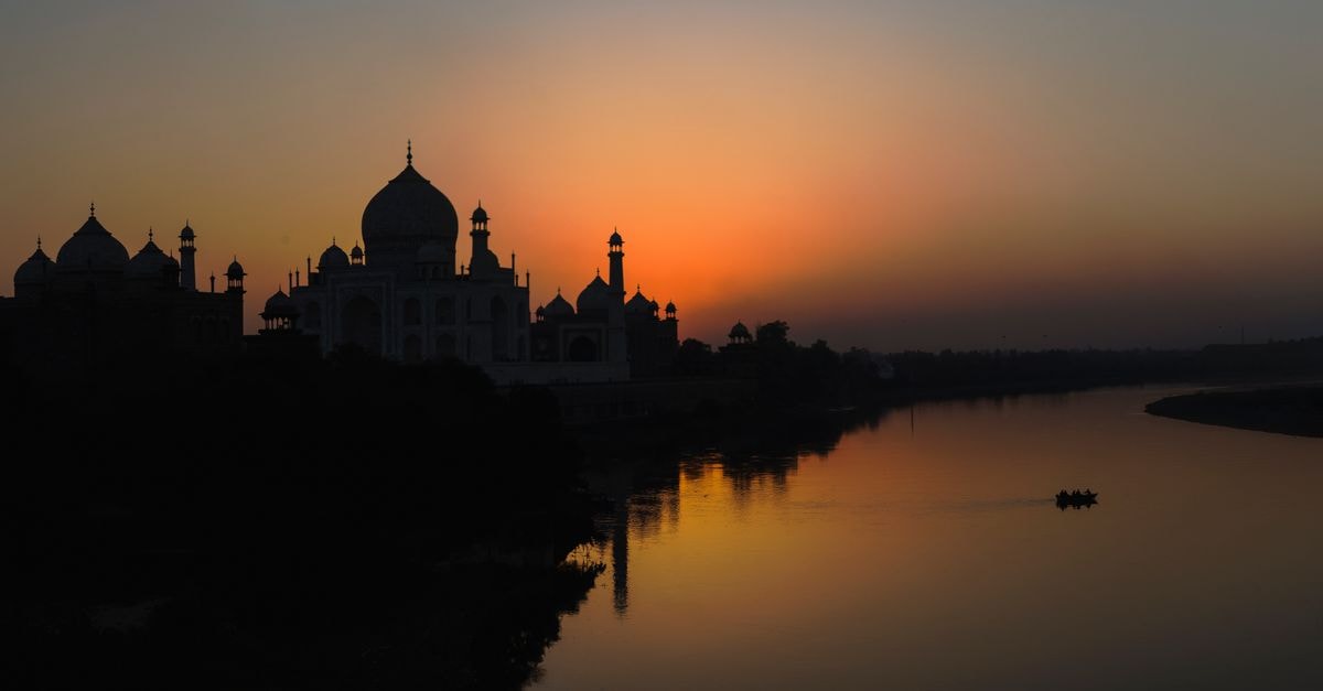 A stunning silhouette of the Taj Mahal at sunset along the Yamuna River, showcasing architectural beauty.