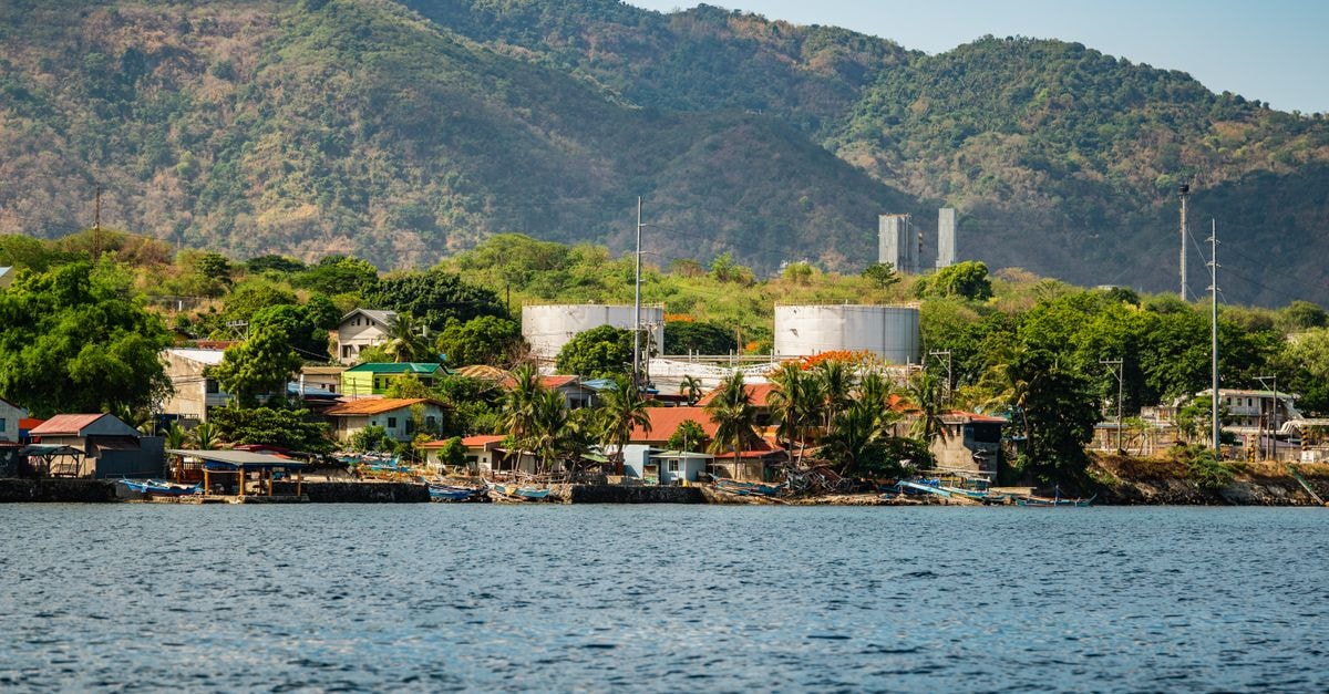 Hotel Dafam Cilacap: A 102-Room Stay Near Teluk Penyu Scenic view of a coastal village with industrial tanks against lush mountains under a clear blue sky.