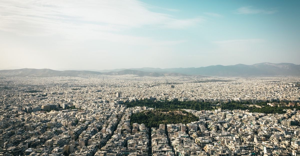 Hotel Astor, Athens — Acropolis Views from a Classic Syntagma Stay Aerial view of Athens cityscape showcasing urban density with mountains in the background.