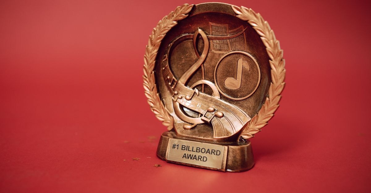 A close-up of a golden music award trophy against a vibrant red background.