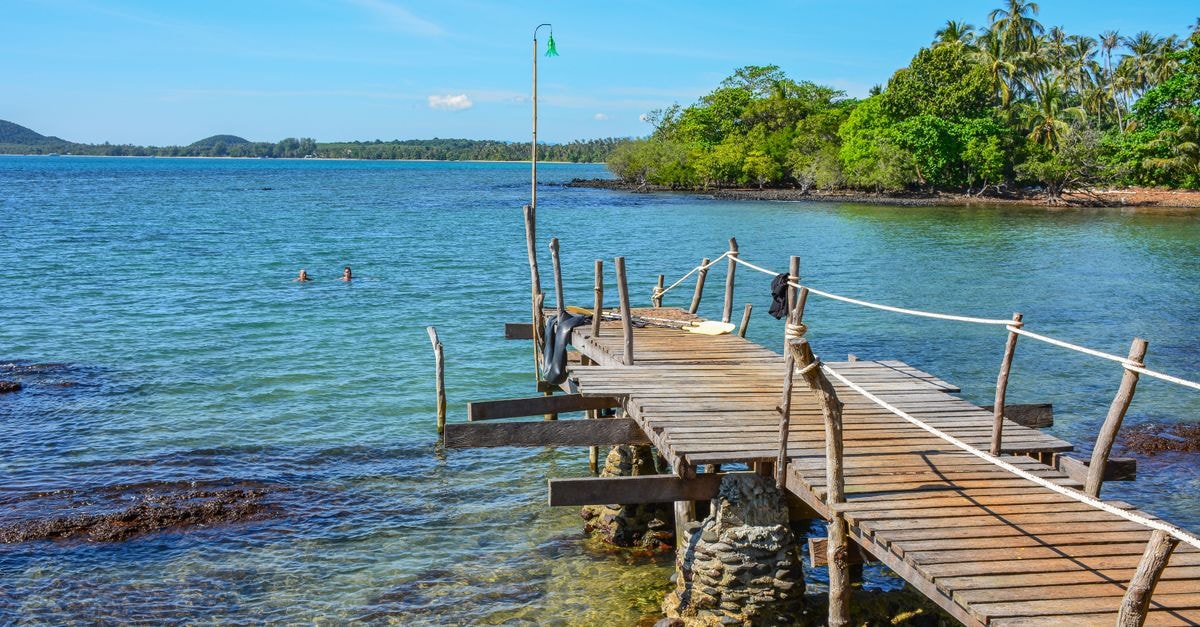 Koh Kong Travel Guide: Planning Tips, Costs and Things to Do Tranquil seaside scene with a rustic pier on Ko Mak, Thailand, under a bright summer sky.
