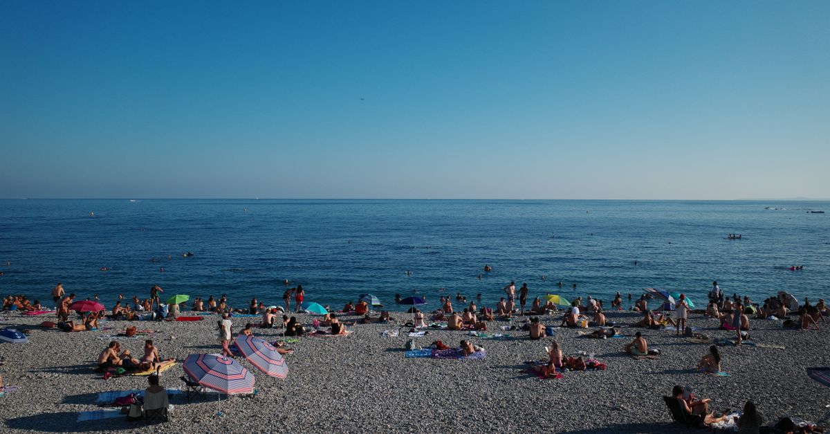 A lively beach scene in Nice, France with sunbathers and umbrellas on a sunny summer day.