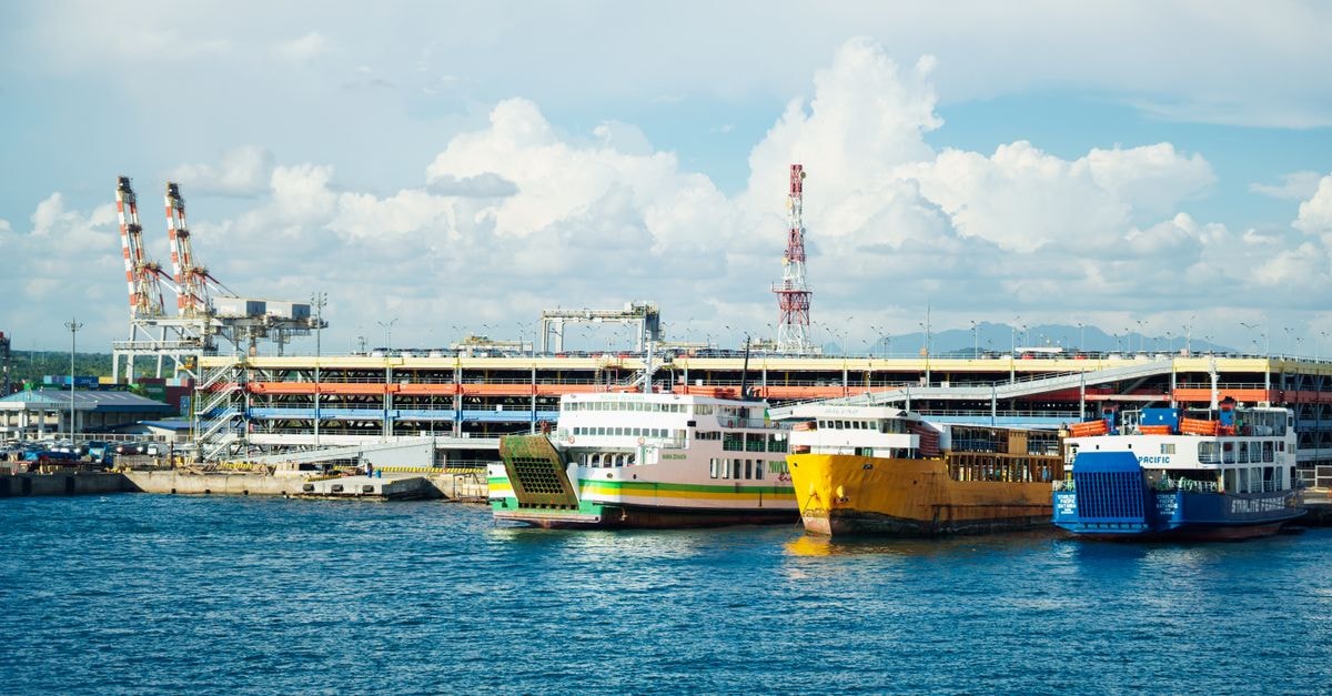 Cilegon Travel Guide: Getting Around and Eating Well in Banten's Industrial Harbor City Vibrant ferries docked at a bustling urban port under a bright sky with scattered clouds.