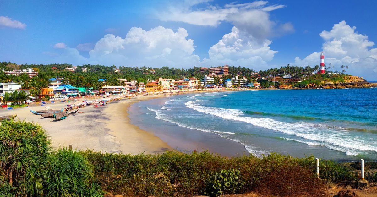 KTDC Grand Chaithram, Thiruvananthapuram — Heritage Capital Stay Beautiful view of Kovalam Beach, India featuring a vibrant town and iconic lighthouse.