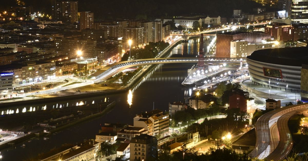 Aerial view of Bilbao cityscape illuminated at night, showcasing vibrant urban life.