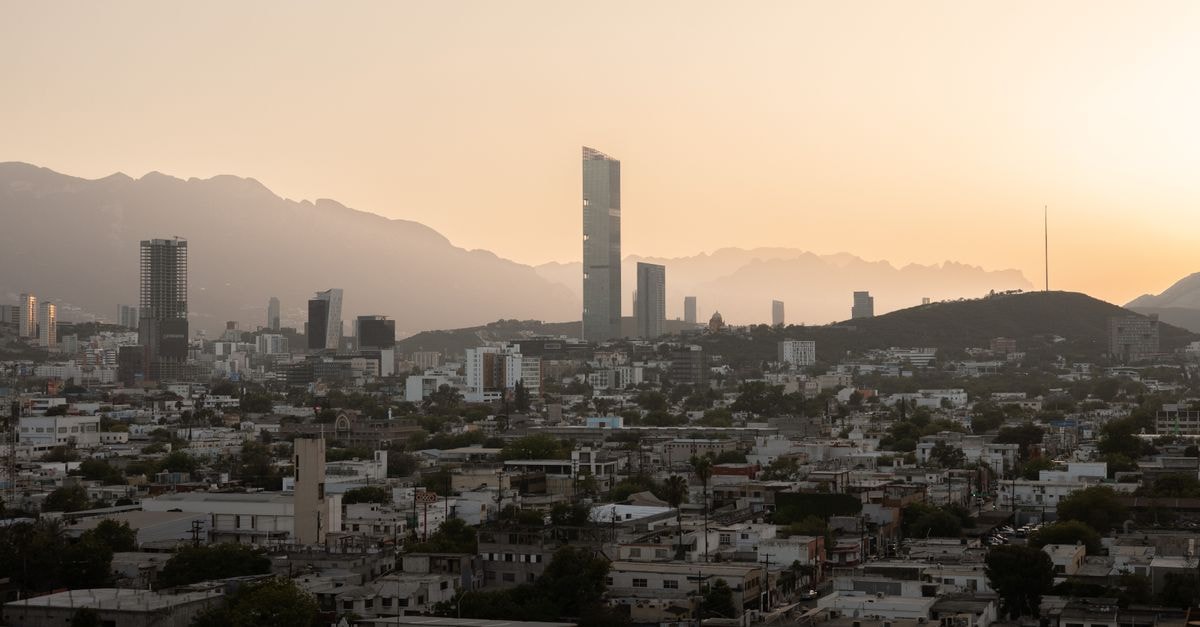 Aerial view of Monterrey's skyline at sunset, featuring modern skyscrapers and mountains.