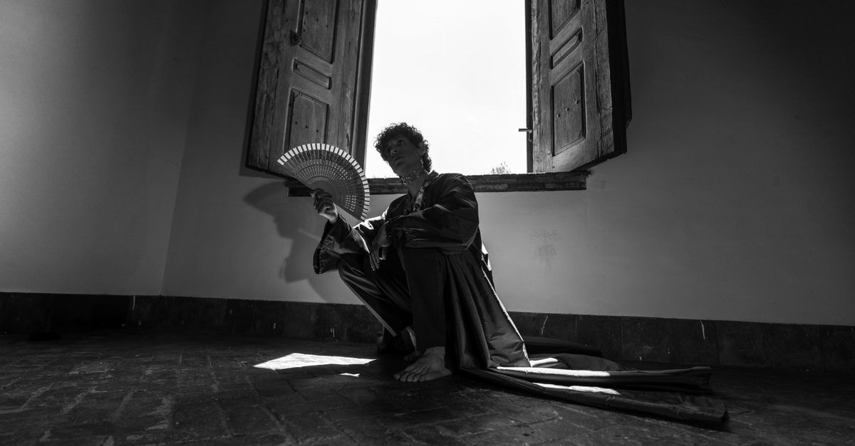 Black and white image of a person with a fan in Leon, Mexico, evoking mystery and calm.