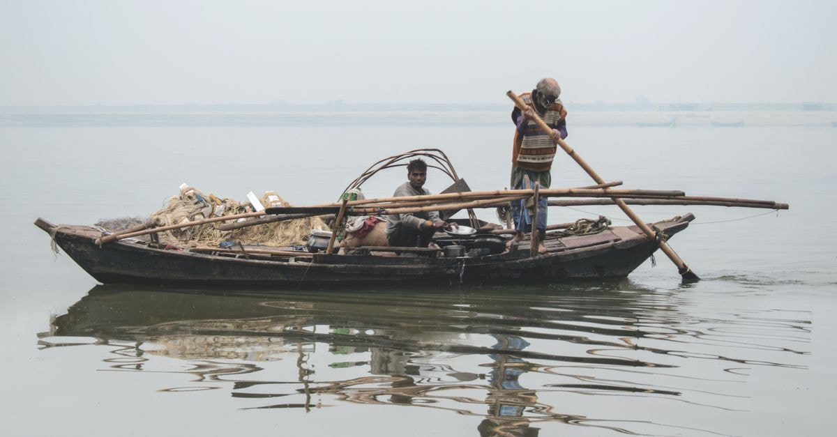 Chiniot Travel Guide: Craft, Markets and River-City Calm Two men on a traditional wooden fishing boat navigating a calm river with oars.