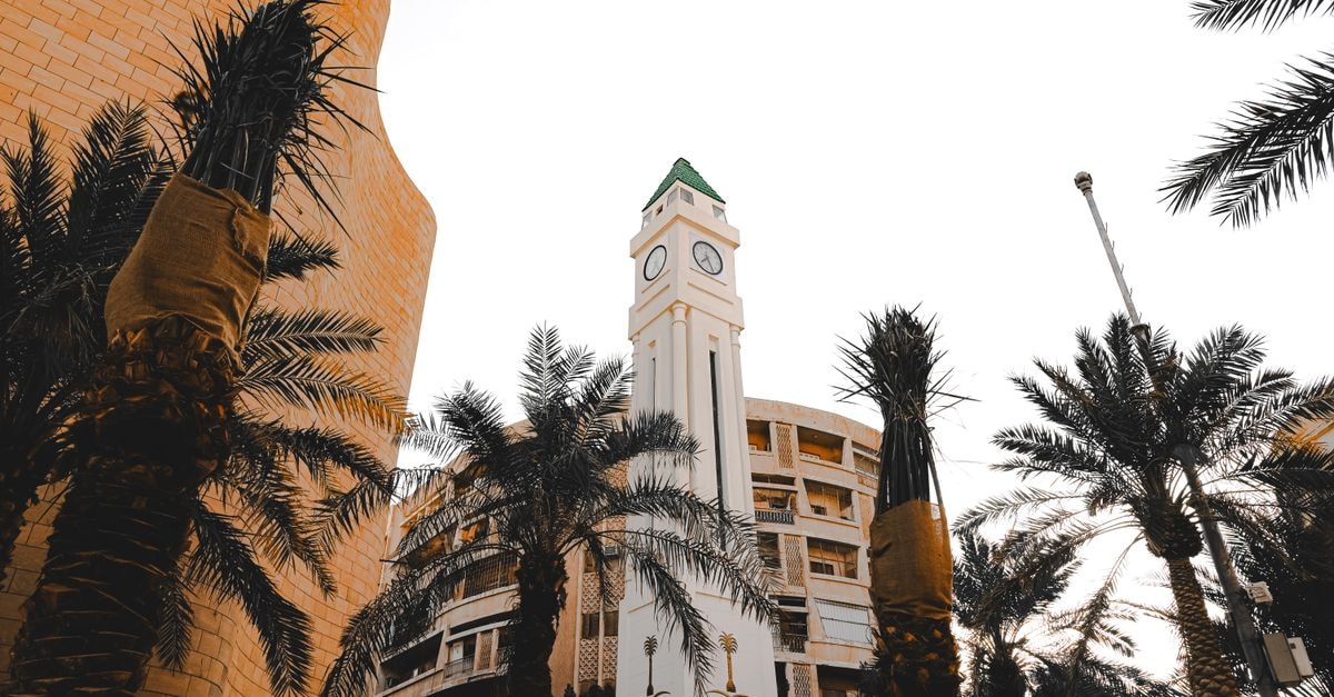 Hyatt Place Riyadh Al Sulaimania in Riyadh: Modern Stay Near Tahlia Street A striking clock tower surrounded by palm trees against a bright sky in an urban environment.