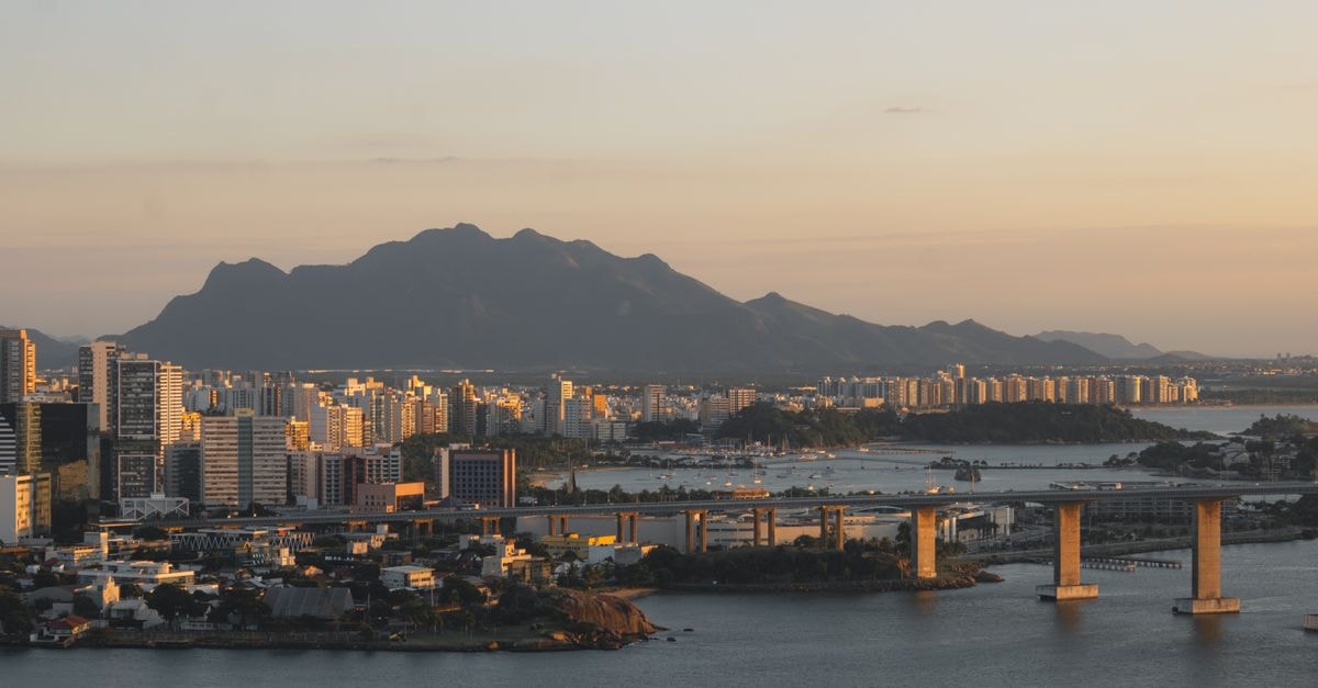 Ibis Budget Santos Gonzaga in Santos: Steps to Gonzaga Beach A serene view of Vitória cityscape at sunset, showcasing the bridge, surrounding buildings, and distant mountains.
