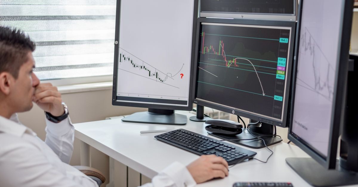 Business professional analyzing financial data on multiple computer monitors at his workspace.
