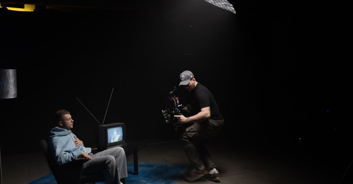 Ted Lasso Season 4 Sets Apple TV+ Launch Record With 296.6 Million Minutes Watched in Two Days A photographer captures a scene with a man sitting next to an old TV in a dimly lit studio.