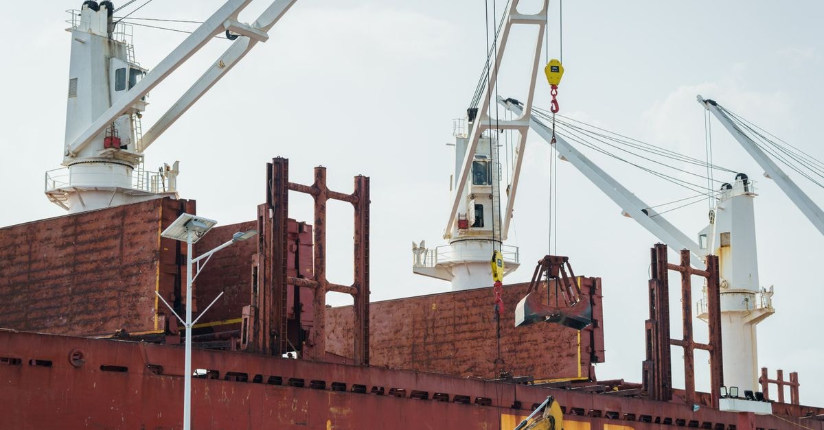 EU steel safeguard reshapes trade flows as Indian exports face 25-30% decline and ArcelorMittal eyes stronger European shipments Cargo ship docked at an industrial port with cranes unloading cargo under clear skies.