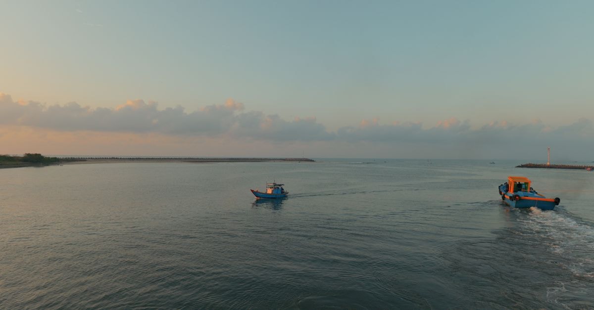 Two small fishing boats navigating serene waters under a soothing sunrise.
