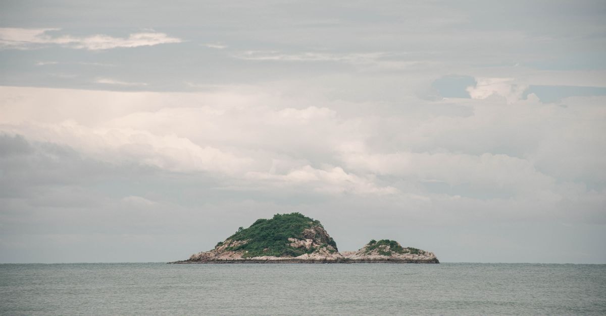 Serene view of a small island surrounded by the sea and cloudy sky in Hua Hin, Thailand.