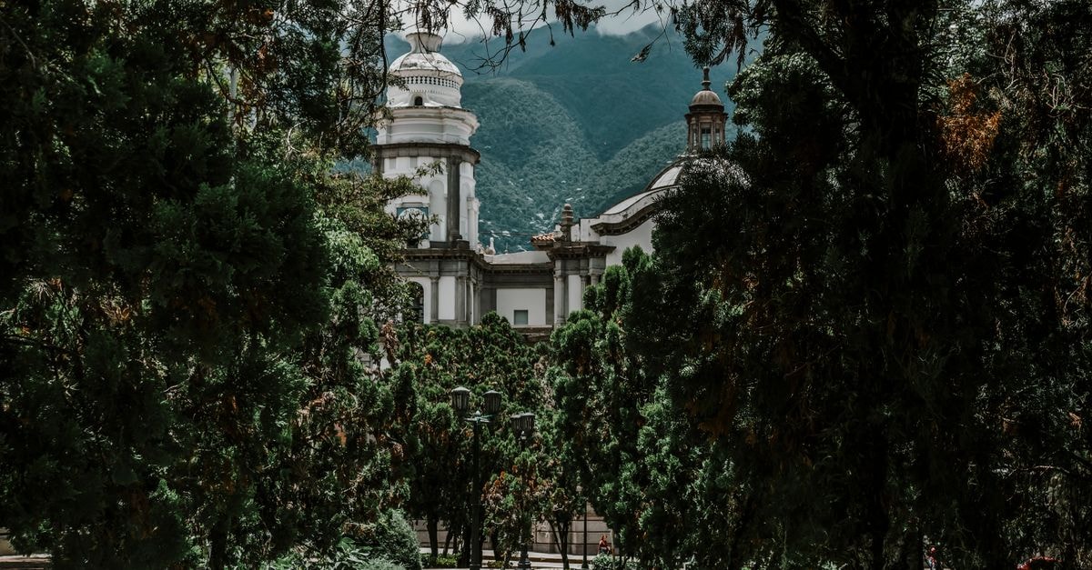 A beautiful historic building in Mérida, Venezuela, enveloped by lush greenery with mountains in the background.