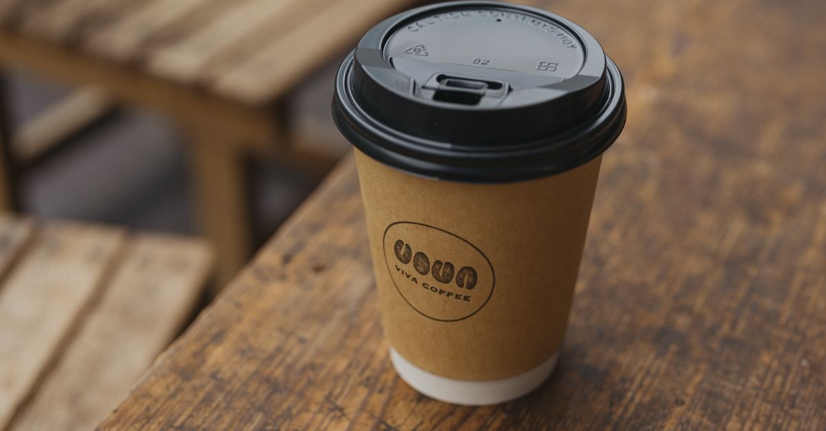 A take-out coffee cup from Viva Coffee on a rustic wooden table in an outdoor cafe setting.