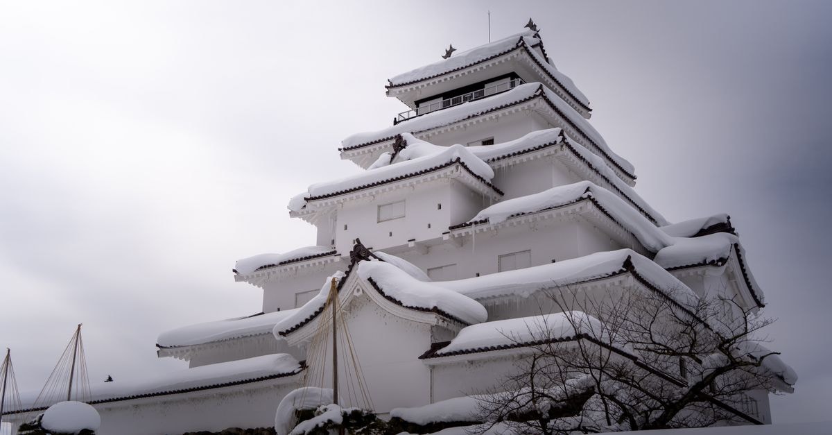 Aizuwakamatsu Travel Guide: Samurai Heritage in the Aizu Basin Aizu-Wakamatsu Castle covered in snow, showcasing traditional Japanese architecture in a winter landscape.