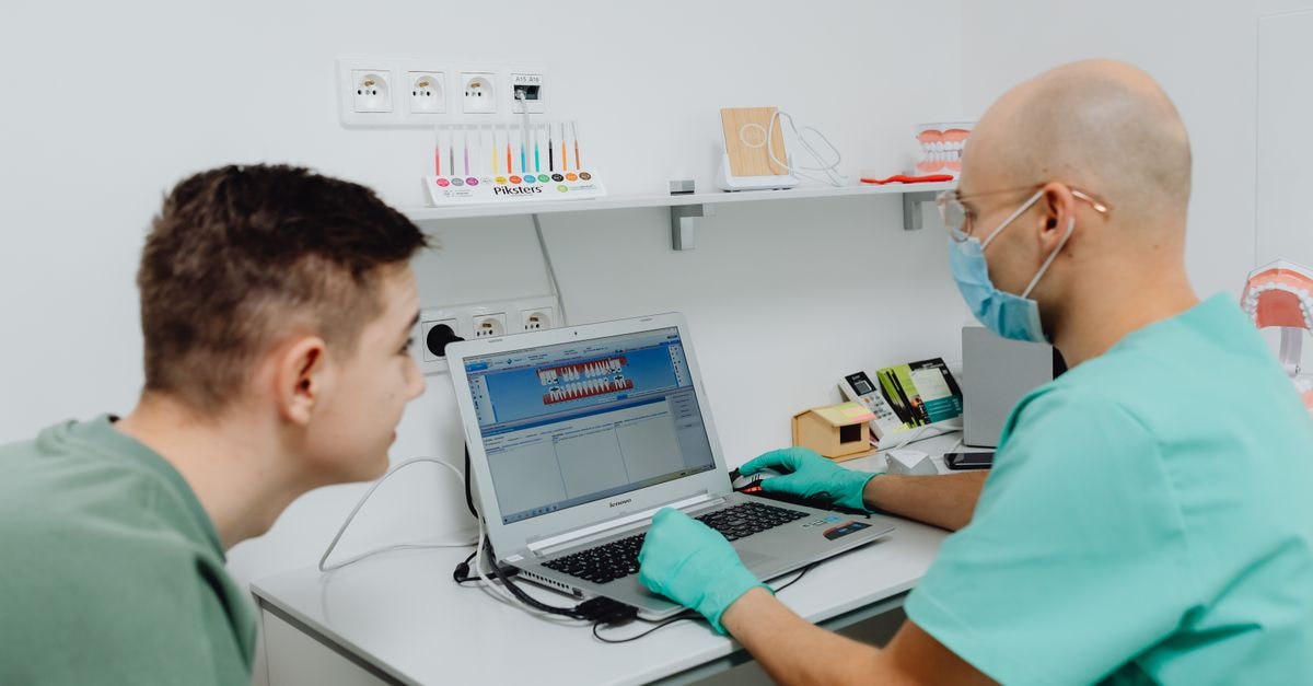 Dentist consulting a patient using laptop in a modern dental clinic setting.