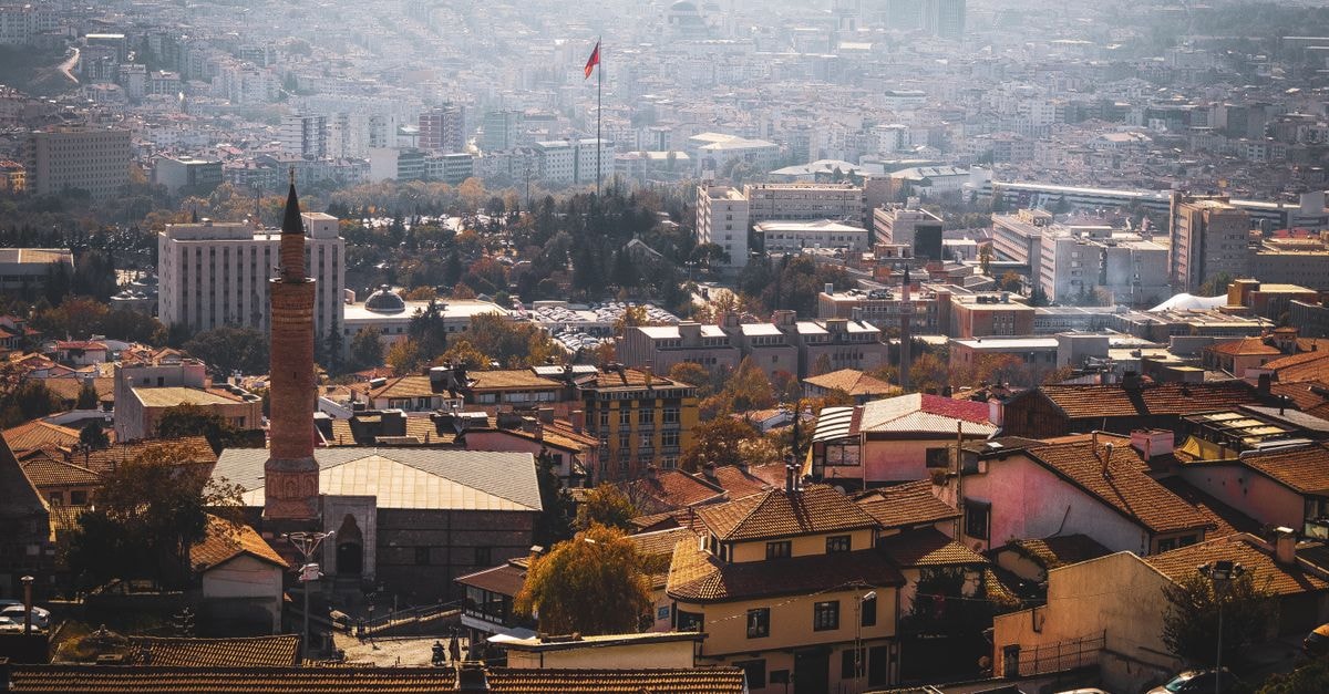 Panoramic view of Ankara cityscape with iconic Turkish flag and mosque amid urban landscape.