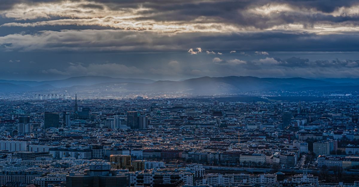 Mercure Vienna First, Vienna — Boutique Base Near the Historic Center A captivating cityscape view with dramatic clouds and sun rays over an urban skyline, showcasing architectural diversity.