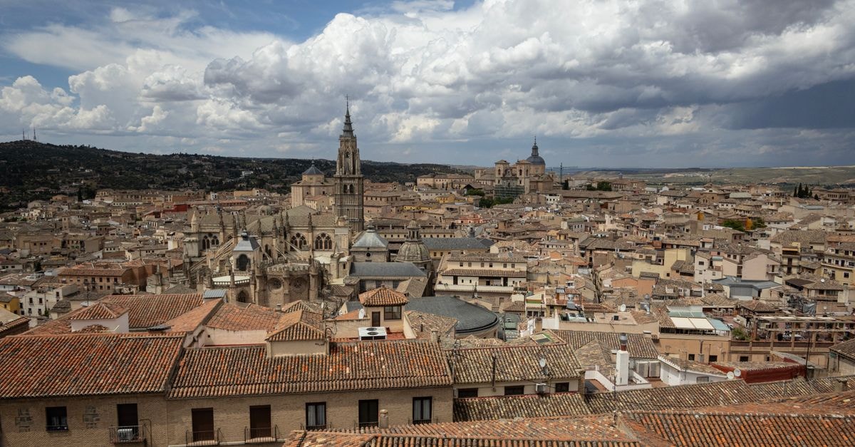 Hotel La Ciudad in La Asunción: A Quiet Posada Near a 17th-Century Castle A breathtaking aerial view of Toledo, Spain showcasing its historic architecture under a dramatic sky.