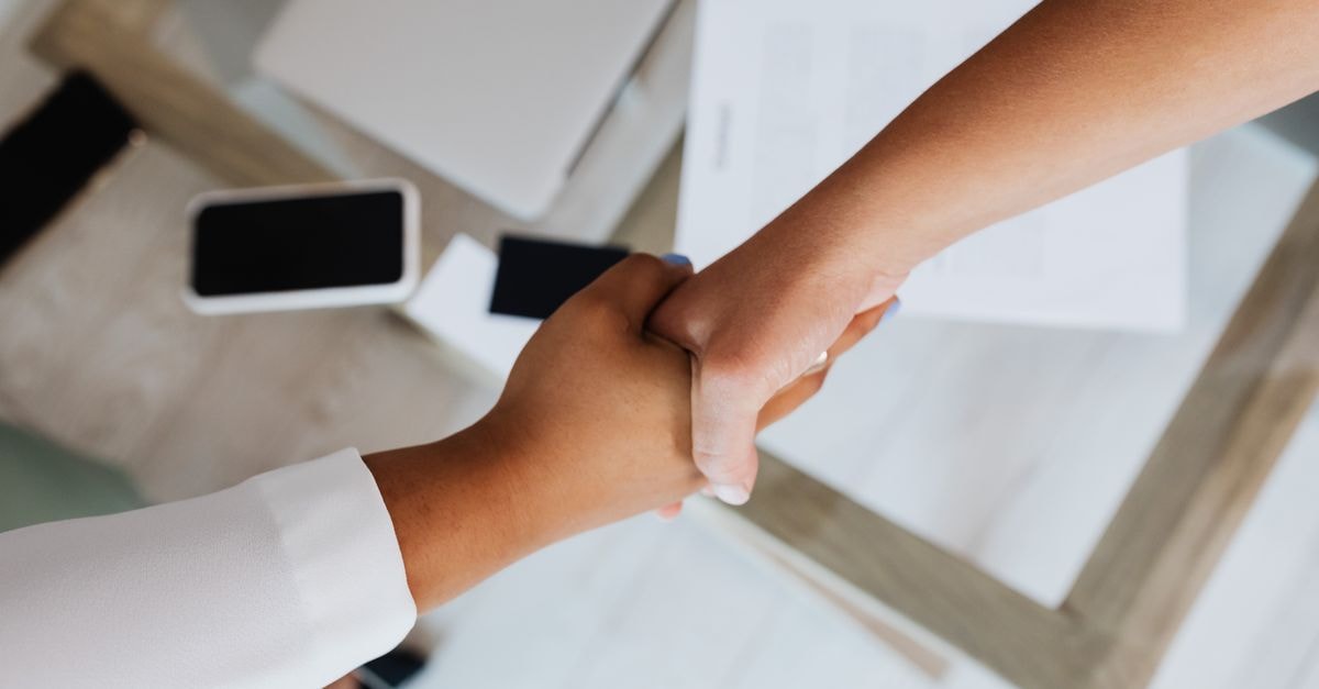 S&P Global’s OpenZeppelin deal extends risk coverage onchain Two people shaking hands over a desk with modern tech, symbolizing a successful business agreement.
