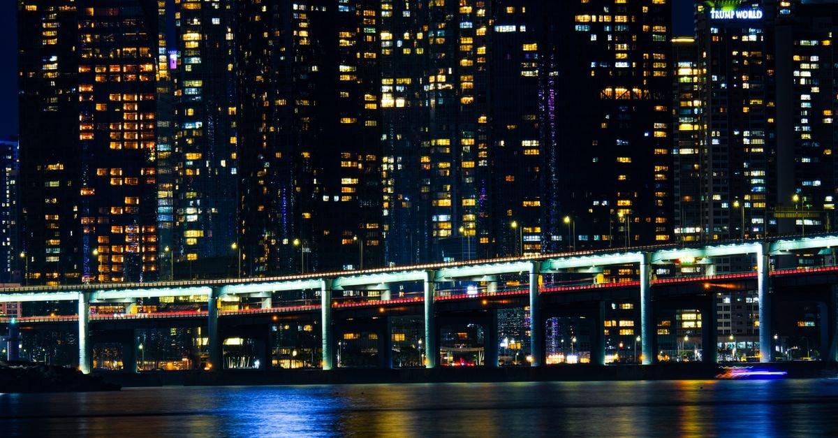 Gwan Moon 1118, Yeosu — A Hostel Steps from Jinnamgwan Hall A glowing city skyline with a bridge reflected in calm waters at night.